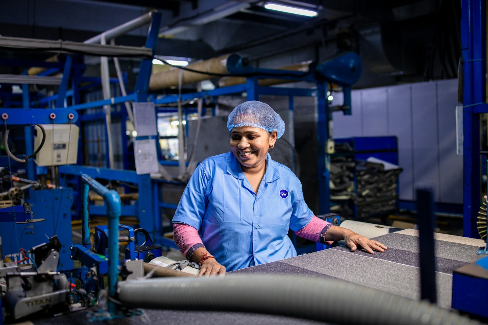 A smiling woman in a hairnet and uniform working at a machine on a bright factory floor