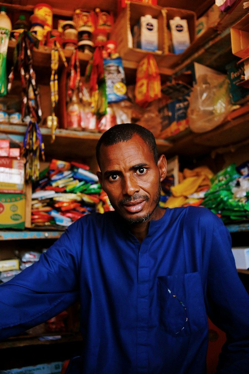 A shopkeeper standing among the shelves of his small convenience shop